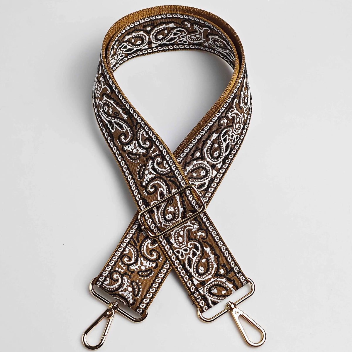 A brown and white paisley jacquard bag strap with a gold buckle and metal hardware.