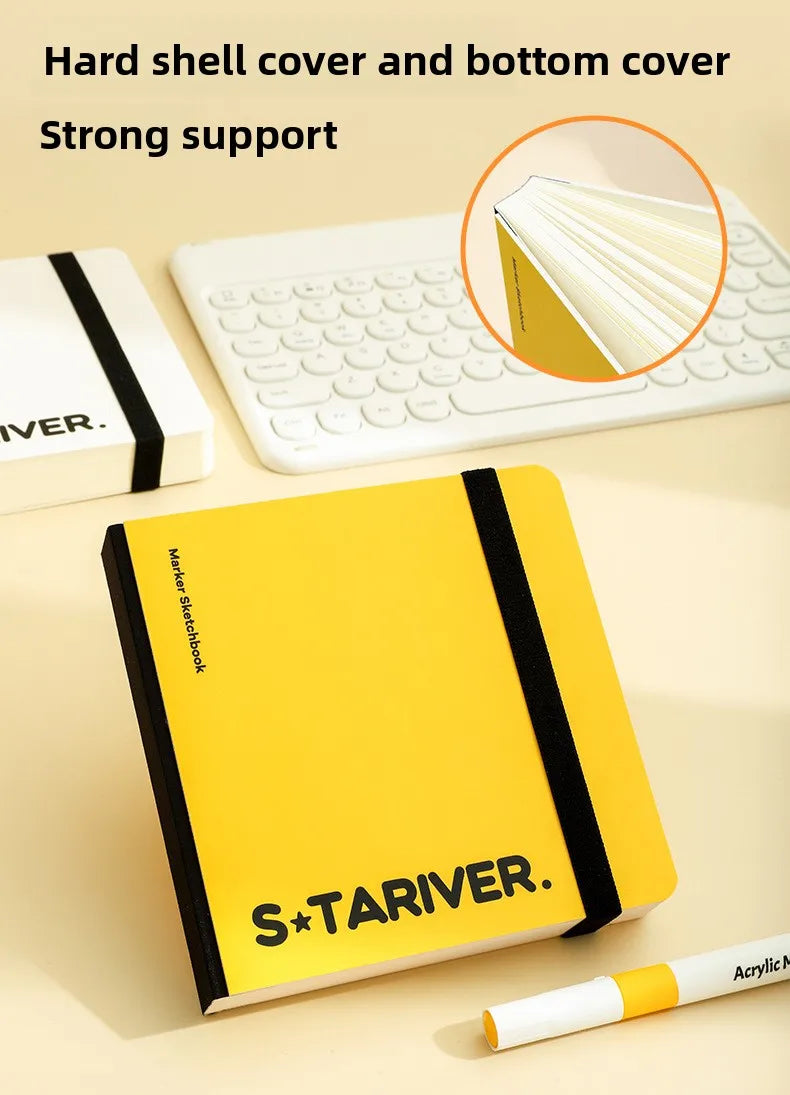 A yellow S&TARIVER sketchbook with a black cover, shown next to a white laptop and an art marker.