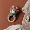 A handmade crochet bunny rattle featuring a natural wood teether ring, set against a brown background.