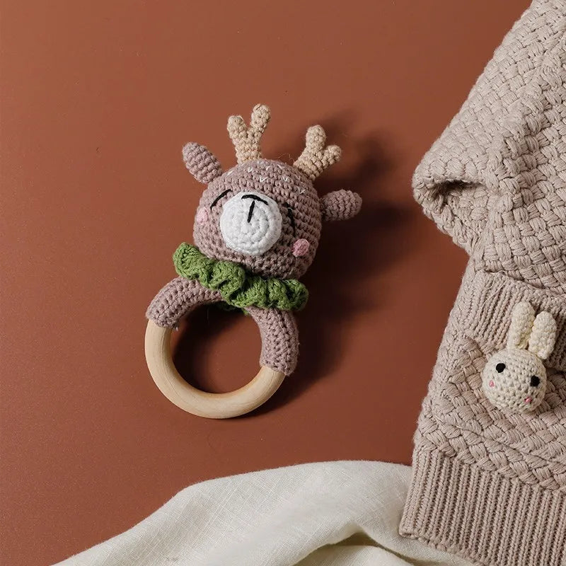 A handmade crochet bunny rattle featuring a natural wood teether ring, set against a brown background.