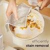 Hands wipe a non-stick pan with a mesh cloth for efficient stain removal.