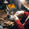 A person wearing white gloves is using a digital microscope to examine small jewelry pieces under bright illumination.
