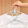 A hand is hanging a white shirt onto a light blue cascading hanger with connector hooks.