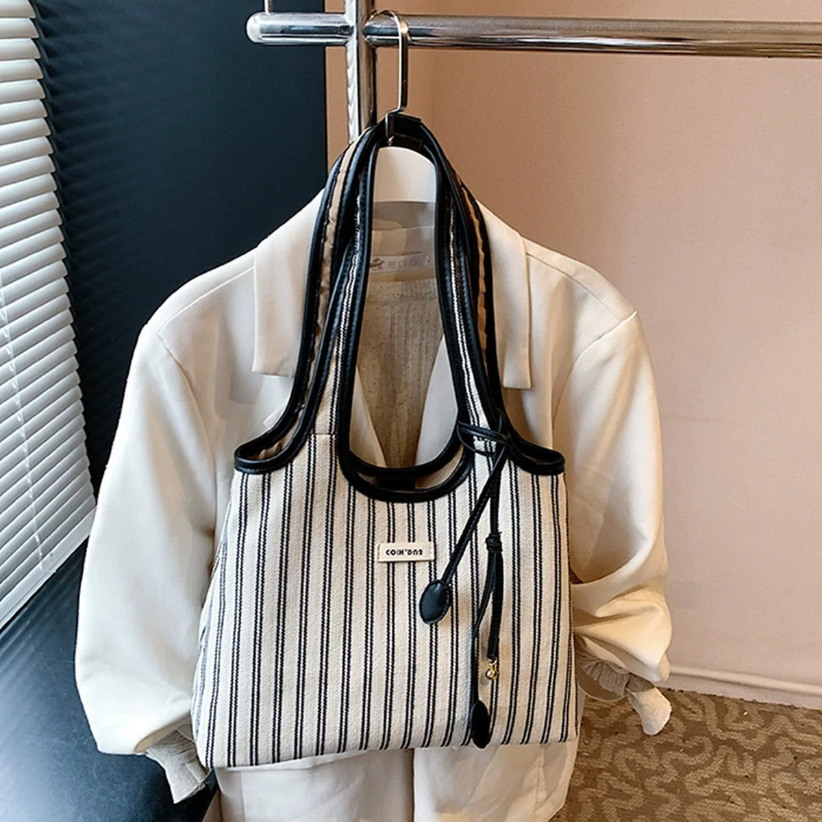 Una camisa blanca colgada en una percha, mostrando una bolsa de lona a rayas con correa cruz para el cuerpo negro.