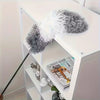 A gray and white extendable microfiber duster with a flexible head resting on a white shelf.