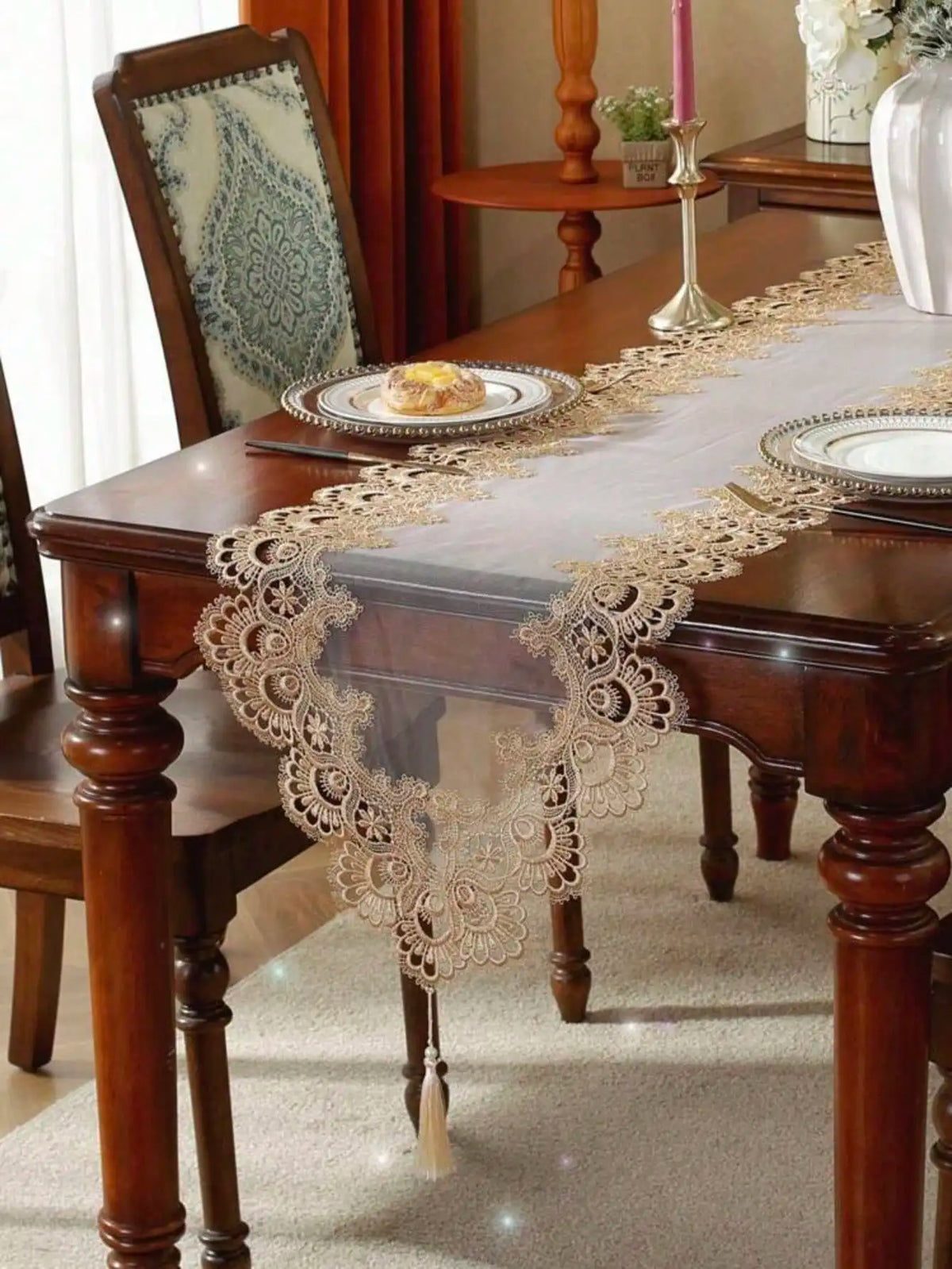 A dark wood table is set with an embroidered mesh lace table runner featuring intricate gold detailing.