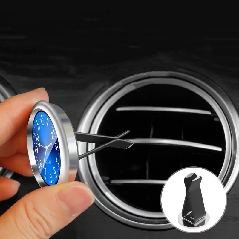 A hand holds a mini car vent quartz clock with luminous hands, showing the watch face and mechanism.