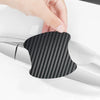 A hand is placing a black carbon fiber protective cover onto a silver car door handle.