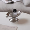 A vintage ceramic soap dish with an elevated stand holding a black glass bottle of Rose of No Man's Land perfume.