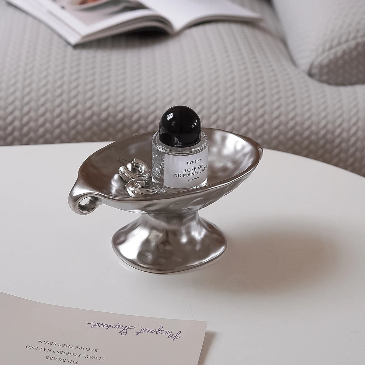 A vintage ceramic soap dish with an elevated stand holding a black glass bottle of Rose of No Man's Land perfume.