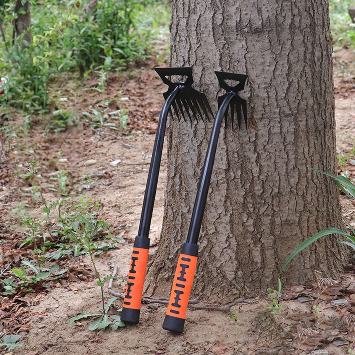 A pair of black stainless steel weeding shovel and rake tools leaning against a tree trunk.