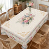 A vintage floral tablecloth is displayed on a dining table surrounded by wooden chairs.