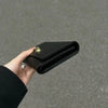 A hand holds a sleek black compact wallet for women, showing the leather texture and gold hardware.