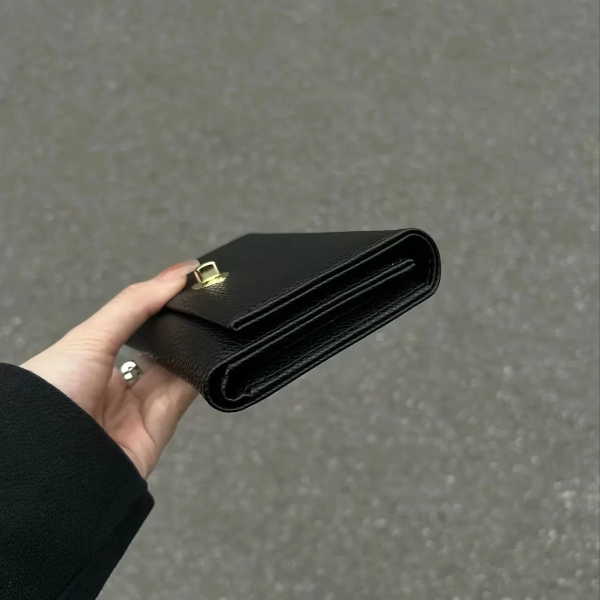 A hand holds a sleek black compact wallet for women, showing the leather texture and gold hardware.