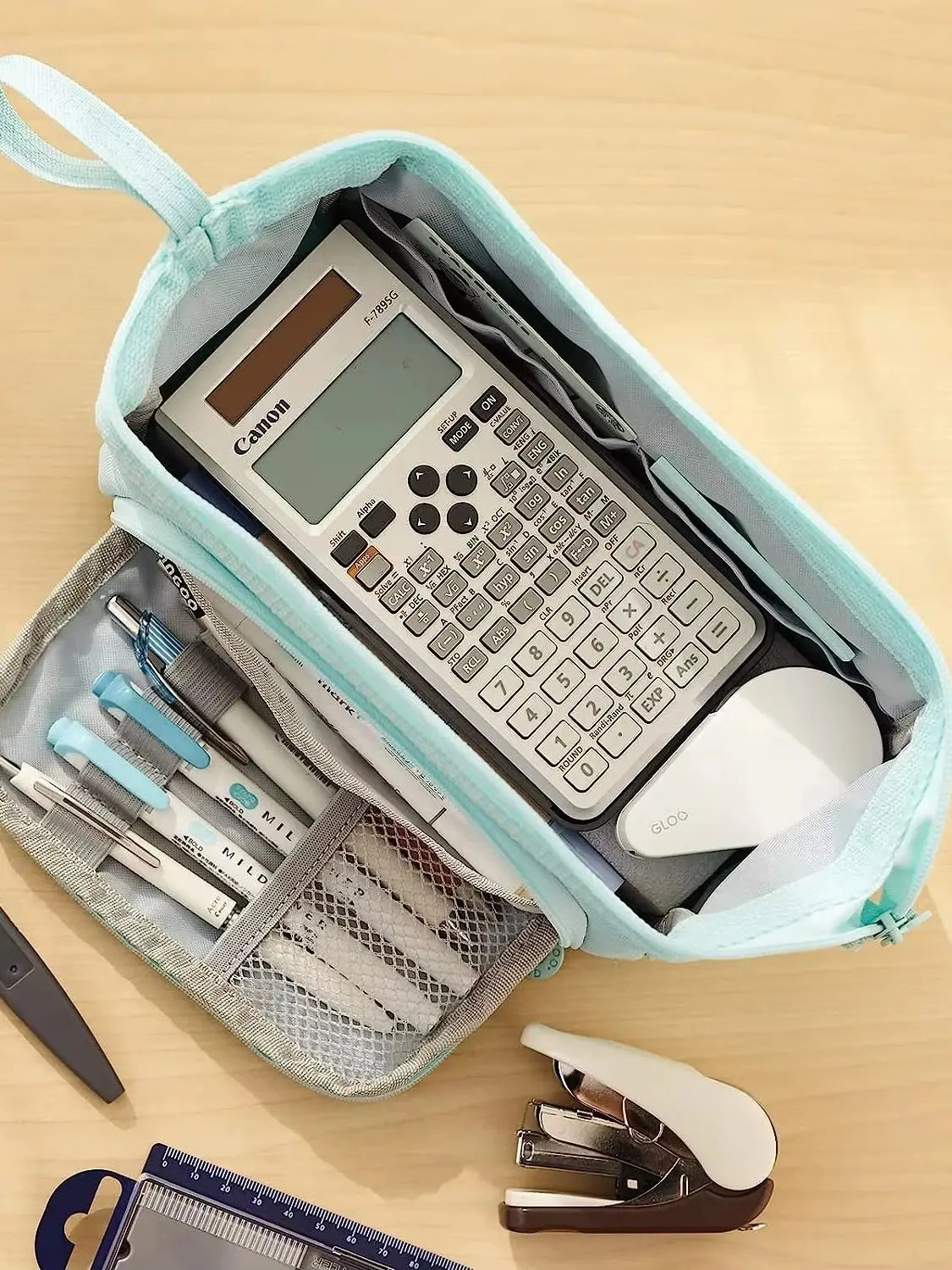 A light blue canvas pencil case is open, revealing a Canon calculator, pens, and a white mouse.