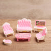 A set of pink miniature dollhouse furniture including a sofa, chairs, and a table on a wooden surface.