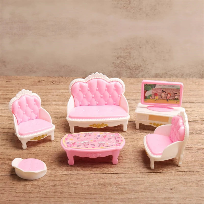 A set of pink miniature dollhouse furniture including a sofa, chairs, and a table on a wooden surface.