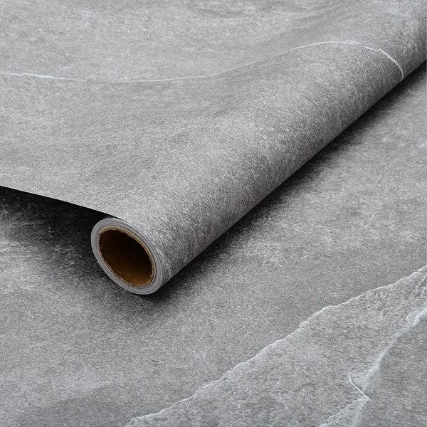 Roll of self-adhesive waterproof floor and wall tiles lying on a gray surface.