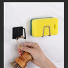 A hand holds a wooden brush attached to a black holder, demonstrating the sponge rack's functionality.