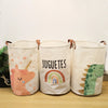 Three white fabric storage baskets with colorful cartoon prints of a unicorn, rainbow, and dinosaur.