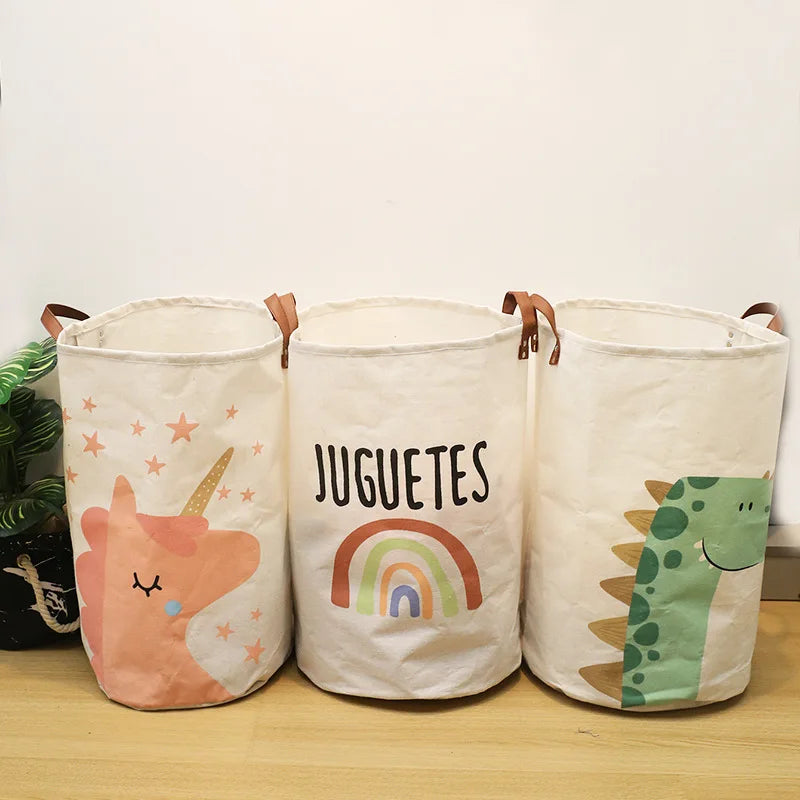 Three white fabric storage baskets with colorful cartoon prints of a unicorn, rainbow, and dinosaur.