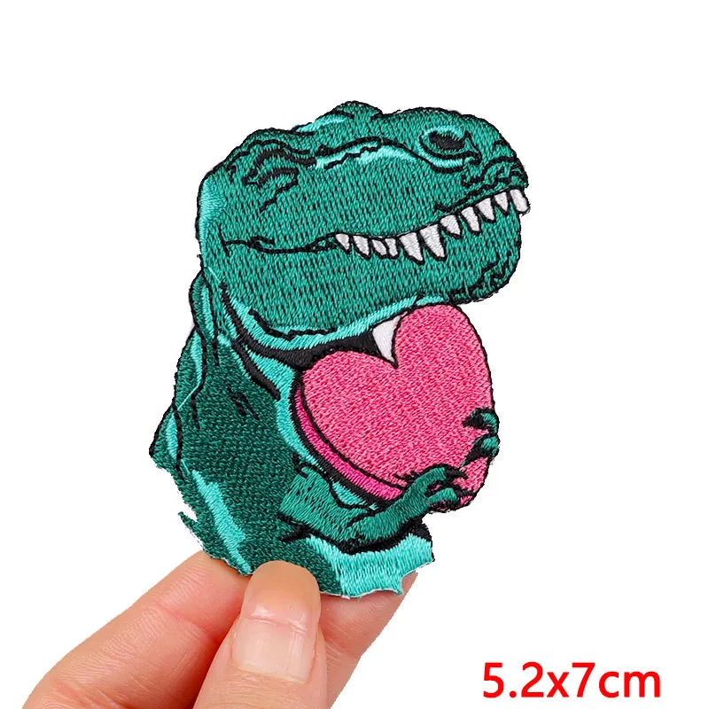 A teal cartoon dinosaur embroidery patch with a pink heart on it.