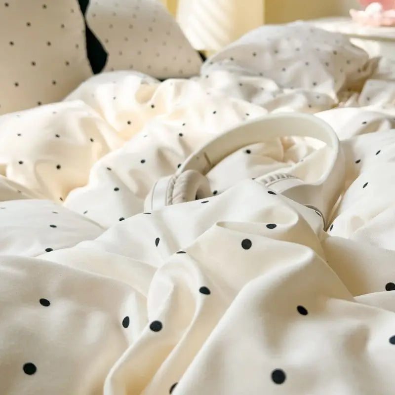 A close-up of a cream-colored polka dot bedding set with a duvet cover and pillow, showing soft folds.