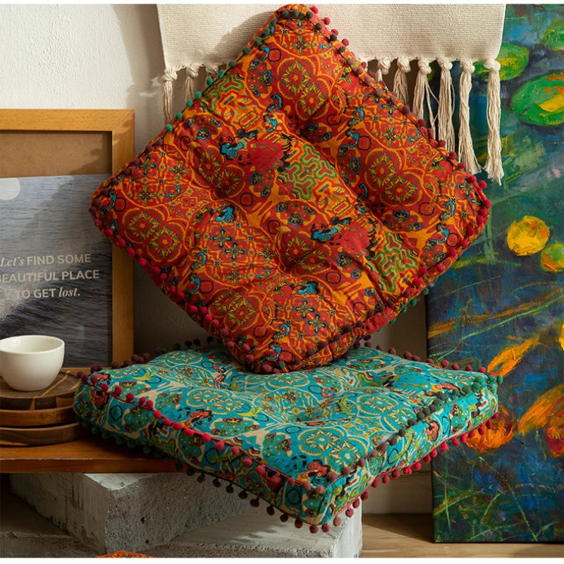 A vibrant orange and red memory foam floor cushion with tassels displayed against a colorful textile background.