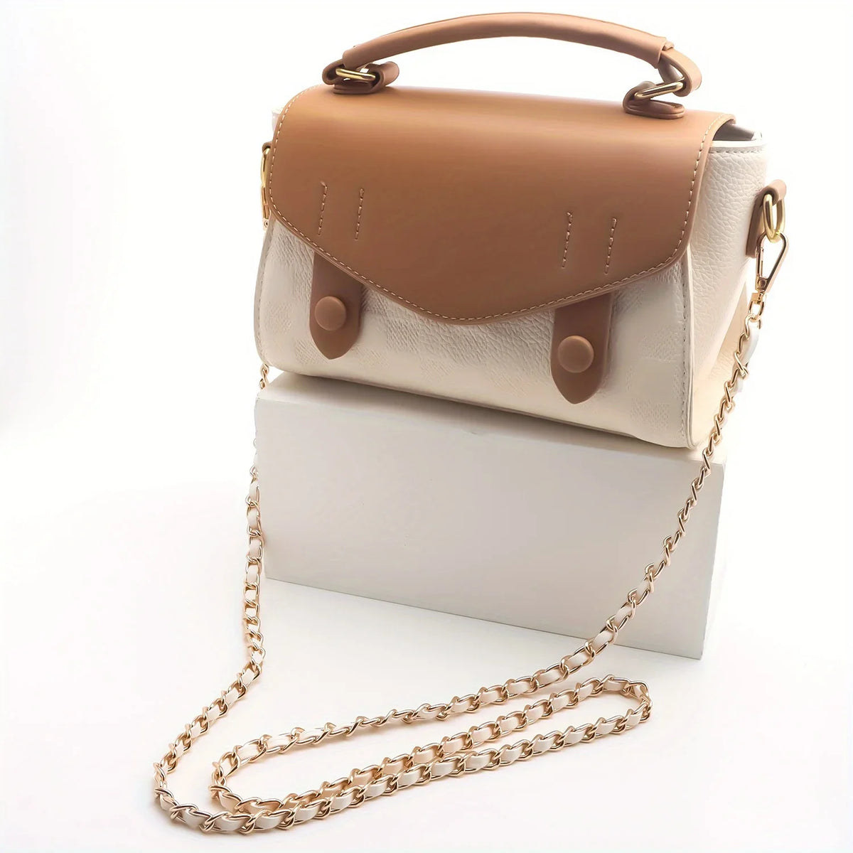 A tan and cream leather purse with a metal chain strap resting on a white box.