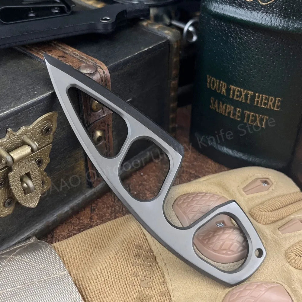 A compact stainless steel neck knife is shown resting on a tan glove and next to a dark box.