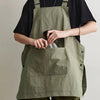 A person wearing a olive green waterproof apron over a black shirt, holding a glass.