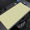 A large beige non-slip desk mat is placed on a dark desk next to a laptop and a potted plant.