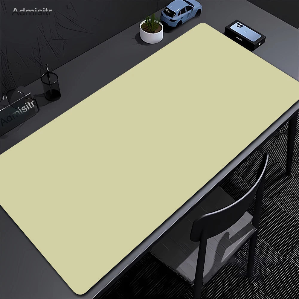 A large beige non-slip desk mat is placed on a dark desk next to a laptop and a potted plant.