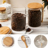 Airtight glass storage jars with bamboo lids and spoons filled with coffee beans on a wooden surface.