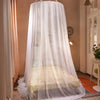 A romantic canopy mosquito net draped over a double bed in a light-colored room.