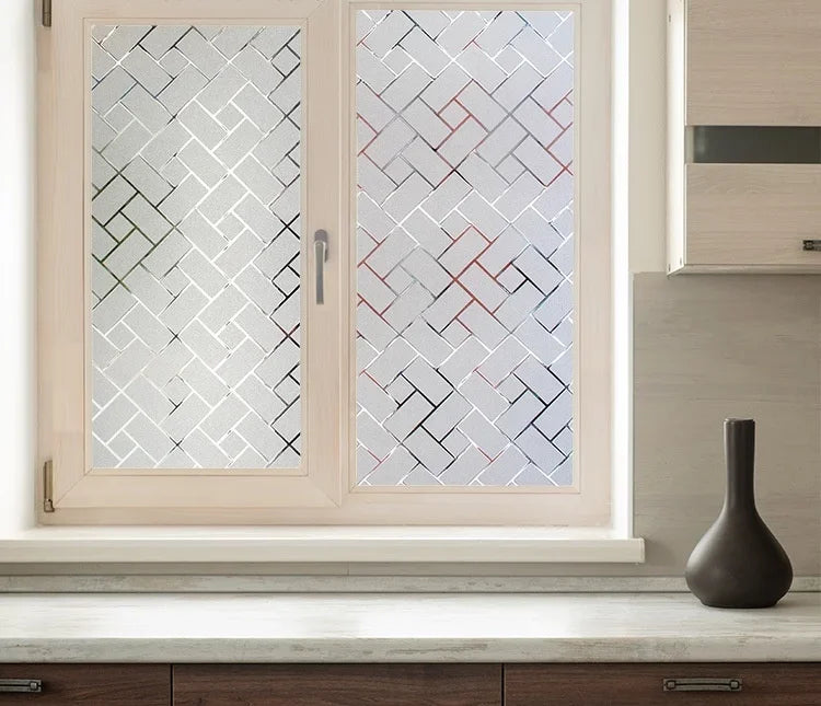 A close-up of a light pink window with decorative frosted privacy film featuring a geometric pattern.