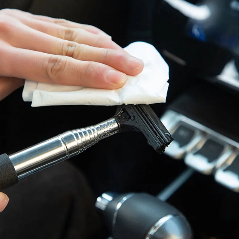 A hand wipes a black retractable car mirror or window cleaning wiper with a white cloth.