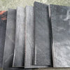 A stack of black buffalo horn knife handle scales, showing various textures and finishes.