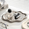 A silver cloud-shaped jewelry tray holding a pair of eyeglasses and a small leather accessory.