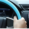 A hand grips a blue silicone steering wheel cover on a car's steering wheel.