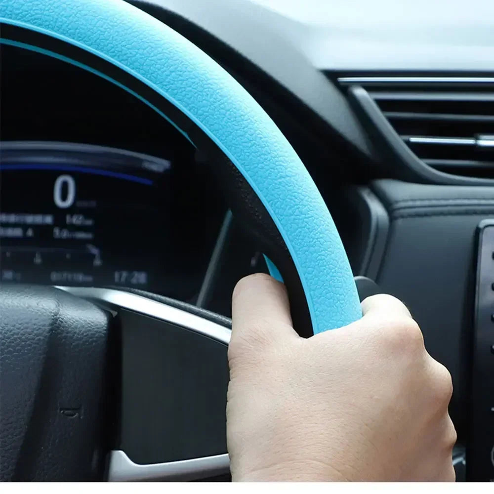 A hand grips a blue silicone steering wheel cover on a car's steering wheel.