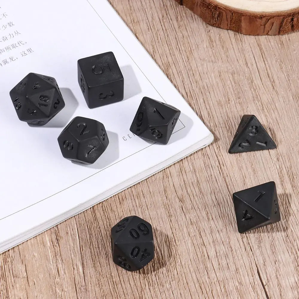 A set of matte black polyhedral dice resting on a white paper next to a wooden surface.