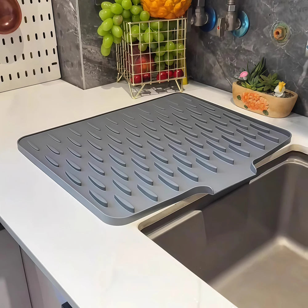 A gray silicone sink drain mat is placed inside a stainless steel kitchen sink.