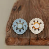 A light blue silicone baby pacifier with a flower design rests on a rustic wooden surface.