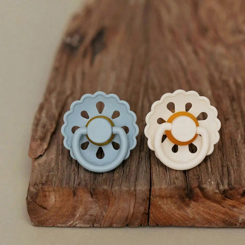 A light blue silicone baby pacifier with a flower design rests on a rustic wooden surface.