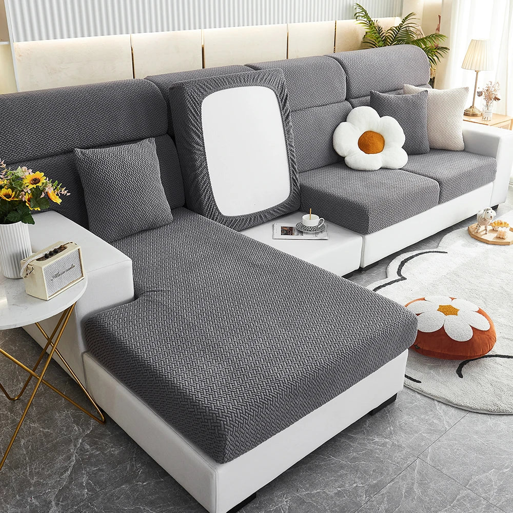 A modern gray sofa slipcover with white cushions and a light wood accent table in a bright living room setting.