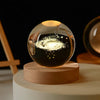 A laser engraved crystal ball night light glowing with golden sparks on a wooden base.