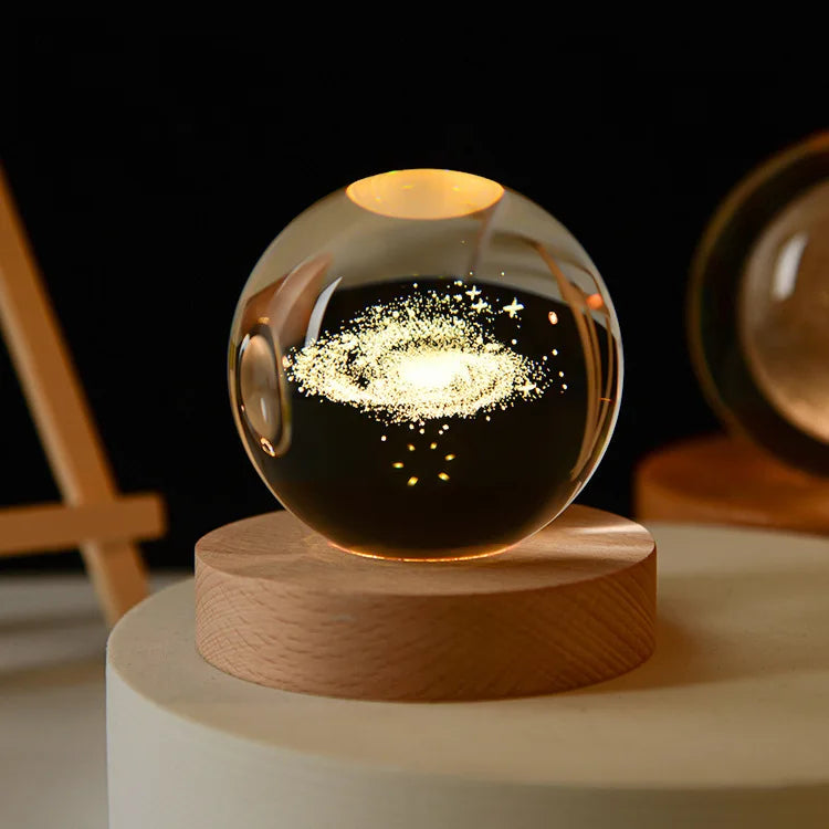 A laser engraved crystal ball night light glowing with golden sparks on a wooden base.