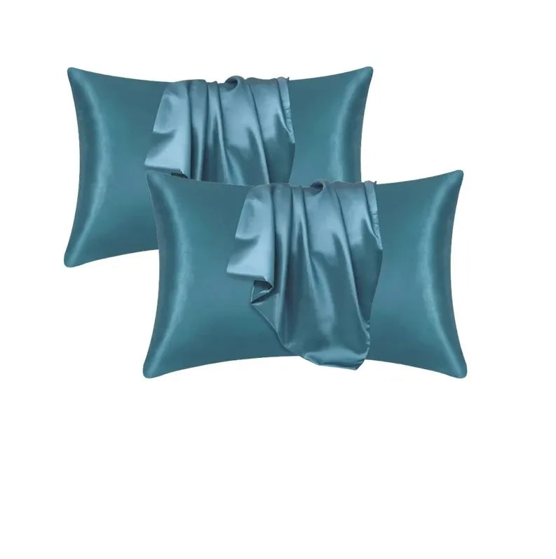 Un par de fundas de almohada de satén seda color verde azulado, dobladas y exhibidas contra un fondo blanco.