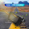 A black solar charging panel device is shown on an asphalt road, demonstrating solar and USB charging capabilities.